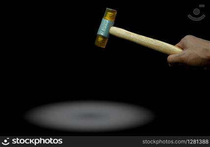 Man&rsquo;s hand holding plastic hammer isolated on dark background. Male worker&rsquo;s hand hold wood handle of plastic hammer. Hammer head made of soft and tough yellow plastic that not damage workpiece.