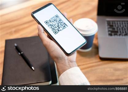 Man's hand holding smartphone with QR code on the screen, payment, E wallet , cashless technology generate digital pay without money. concept