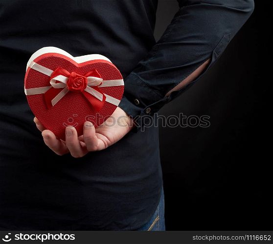 man&rsquo;s hand holds a cardboard red box with a bow behind his back, a man wearing a black shirt, a concept of surprise