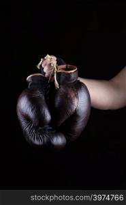 man&rsquo;s hand holds a pair of old leather brown boxing gloves, black background