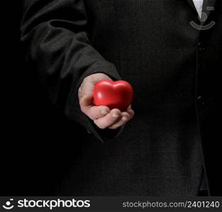 man&rsquo;s hand holds a red heart on a dark background, close up