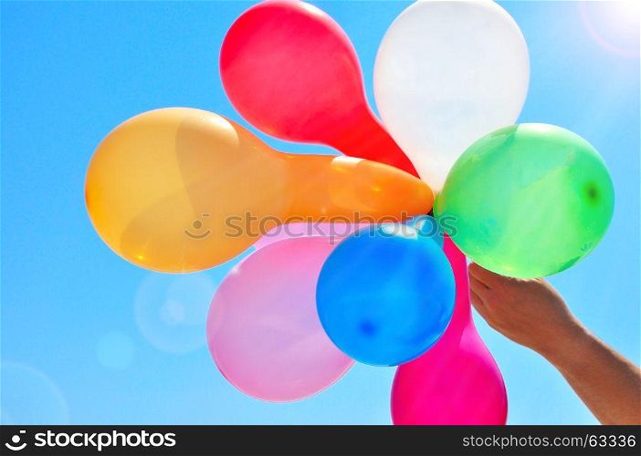 Man's hand holds multicolored balloons against the sky in the rays of the sun