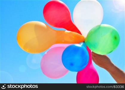 Man's hand holds multicolored balloons against the sky in the rays of the sun