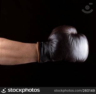 man's hand is wearing a brown leather boxing glove, black background