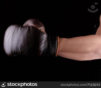 man&rsquo;s hand is wearing a brown leather boxing glove, black background