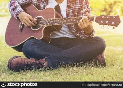 Man &rsquo;s hand playing guitar, sitting on green grass. Nature background. Music, guitar and nature. Country folk song from acoustic guitar. Man holding his guitar.