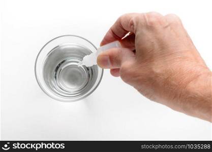 Man&rsquo;s hand putting drops of pharmacy in a glass of transparent water, on white background