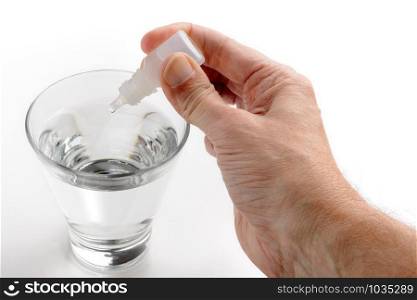 Man&rsquo;s hand putting drops of pharmacy in a glass of transparent water, on white background