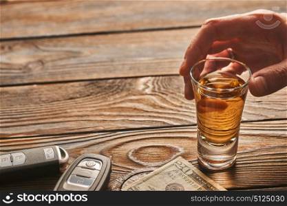 Man&rsquo;s hand reaching to glass of tequila or alcohol drink and car key on rustic wooden table. Drink and drive and alcoholism concept. Safe and responsible driving concept.