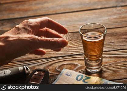 Man&rsquo;s hand reaching to glass of tequila or alcohol drink and car key on rustic wooden table. Drink and drive and alcoholism concept. Safe and responsible driving concept.