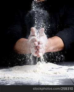 man's hands and splash of white wheat flour on a black background