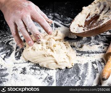 man's hands knead white wheat flour dough on black wooden background