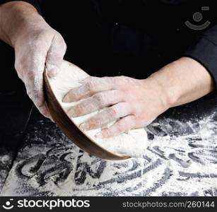 man's hands knead white wheat flour dough on black wooden background, close up