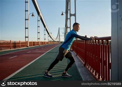 Man runner doing stretching workout before running marathon in urban bridge city background. Man runner doing stretching workout before running marathon