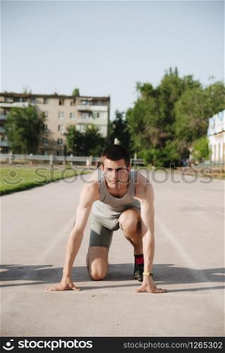 Man runner on start position at stadium. Runner in start pose on running surface. Man run outdoor at running track.. Sportsman on concentrated face ready to go.. young runner athlete in the low start position on the sports track on stadium outdoor