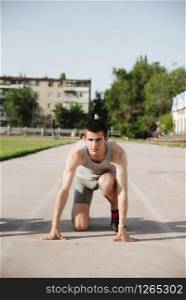 Man runner on start position at stadium. Runner in start pose on running surface. Man run outdoor at running track.. Sportsman on concentrated face ready to go.. young runner athlete in the low start position on the sports track on stadium outdoor