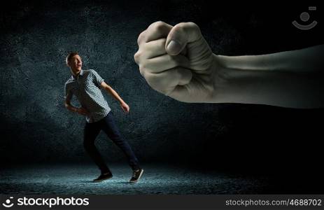Man running away. Funny image of young man trying to escape from huge hand
