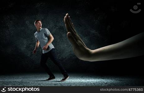 Man running away. Funny image of young man trying to escape from huge hand