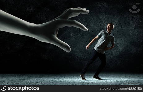 Man running away. Funny image of young man trying to escape from huge hand