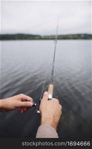 man s hand holding fishing rod front lake