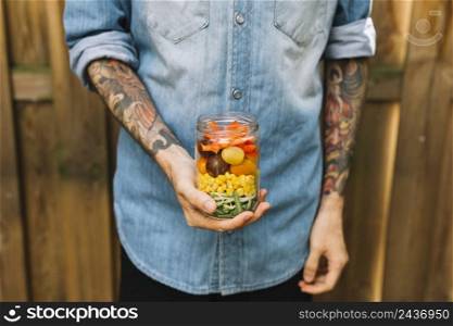 man s hand holding open jar with pasta salad