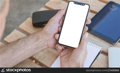 man s hand holding smartphone with blank white screen wooden table