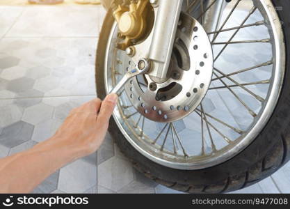 Man’s hand is holding a wrench to tighten the nut of the motorcycle’s lower disc brake pump.