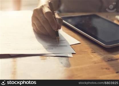 man's hand signing application form with tablet on wooden table, selective focus and vintage tone