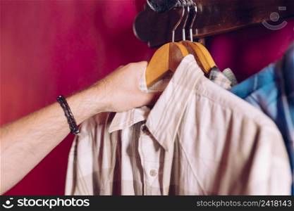 man s hand taking coat hanger shirt from rack hook red wall