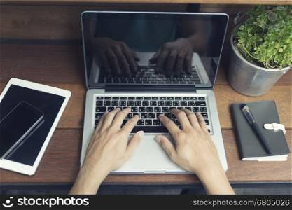 man's hand typing on laptop computer with smartphone and digital tablet on wooden table, selective focus and vintage tone