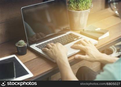 man's hand typing on laptop computer with smartphone and digital tablet on wooden table, selective focus and vintage tone