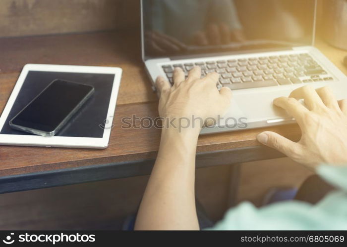 man's hand typing on laptop computer with smartphone and digital tablet on wooden table, selective focus and vintage tone