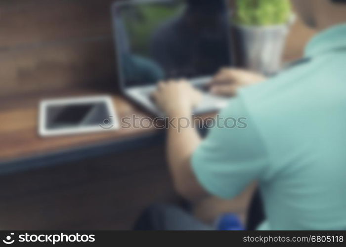 man's hand typing on laptop computer with smartphone and digital tablet on wooden table, blur and defocused