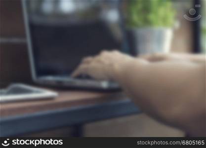 man's hand typing on laptop computer with smartphone and digital tablet on wooden table, blur and defocused