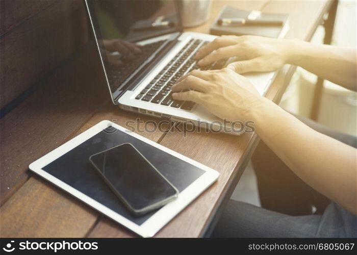 man's hand using smartphone with digital tablet on wooden table, selective focus and vintage tone