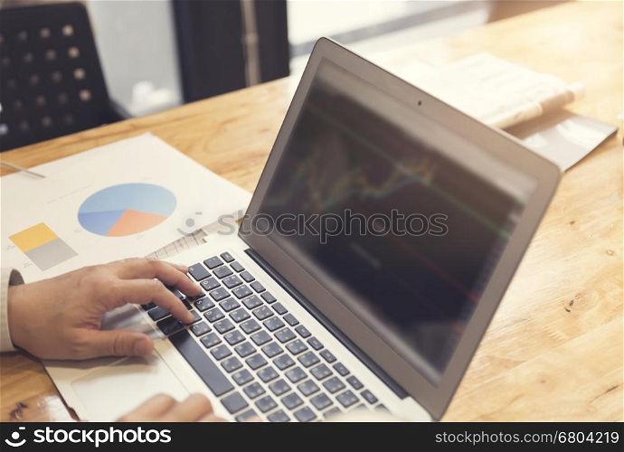 man's hand working with laptop computer with business document on wooden table, selective focus and vintage tone