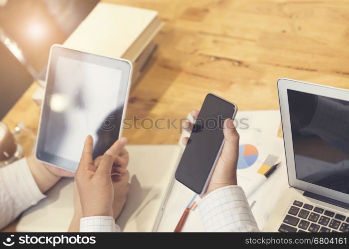 man's hand working with mobile phone, tablet, business document and laptop computer notebook for working concept, selective focus and vintage tone