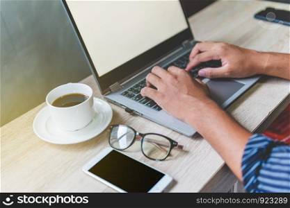 Man?s hands typing on a laptop that is on a wooden desk with a mug of coffee alongside