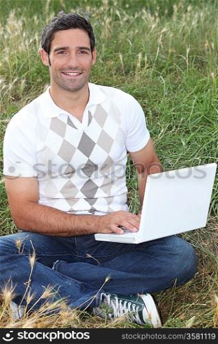 Man sat in field using laptop computer