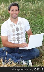 Man sat in field using laptop computer