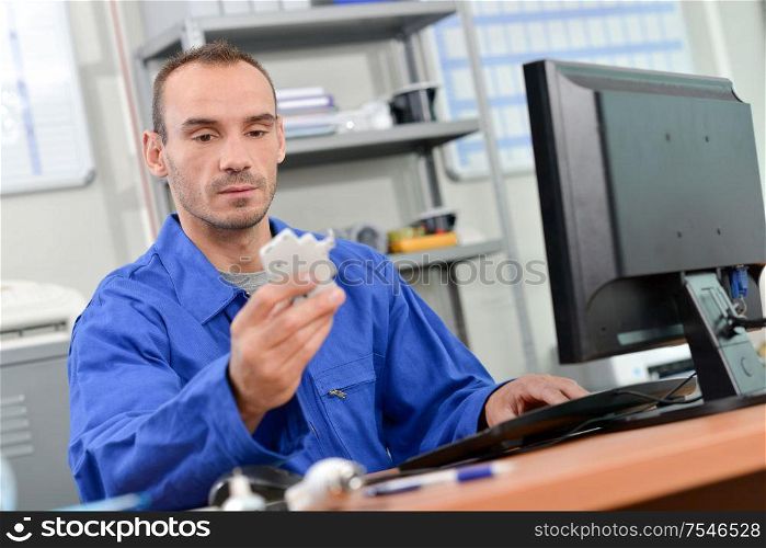 Man sat in front of computer, holding electrical component