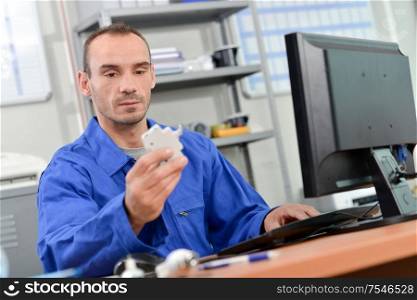 Man sat in front of computer, holding electrical component