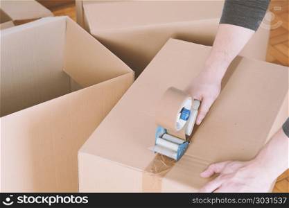 Man sealing a shipping cardboard box with tape dispenser. Indoors. Man sealing a shipping cardboard box
