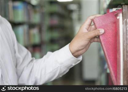 man searching book from textbook shelf in aisle in library