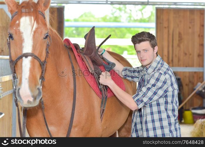 Man securing saddle on horse