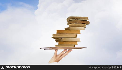 Man serve books. Hand holding tray with pile of old books