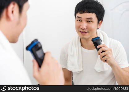 man shaving his face finished and holding electric shave in the bathroom mirror