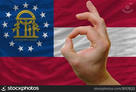 man showing excellence or ok gesture in front of complete wavy american state flag of georgia symbolizing best quality, positivity and succes