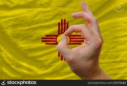 man showing excellence or ok gesture in front of complete wavy american state flag of new mexico symbolizing best quality, positivity and succes