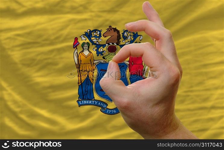 man showing excellence or ok gesture in front of complete wavy american state flag of new jersey symbolizing best quality, positivity and succes